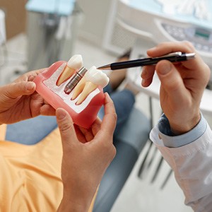 Dentist pointing to model of dental implant held by dental patient